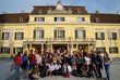 Many students from all around the world standing in front of yellowish old building in Laxenburg and waving to camer