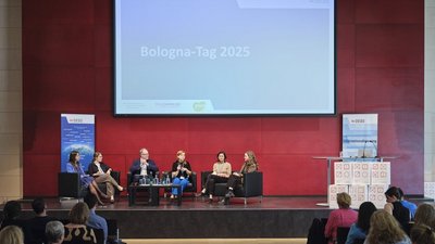 Sechs Personen sitzen auf einer Bühne und diskutieren gemeinsam