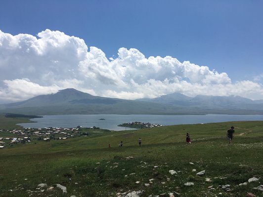 People walking on vast meadow and a big lake with some houses next to it