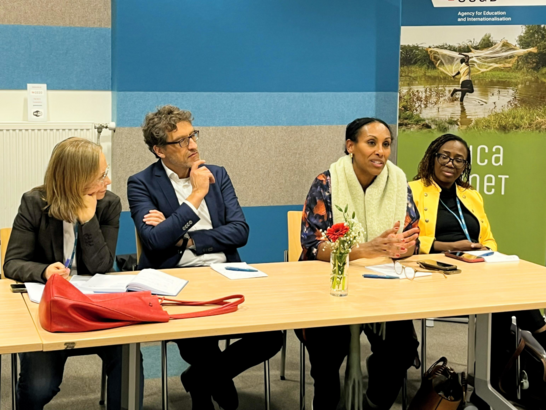 Four participants sitting at a table, one woman is talking