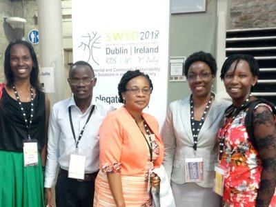 Five people posing for a group photo in front of a big conference poster