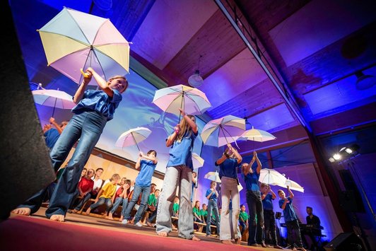Kinder stehen auf einer Bühne, sie halten Regenschirme