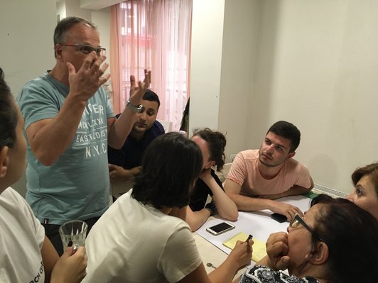 Group of sitting people are looking at a man who ist standing and talking about something