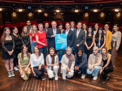 The OeAD managing director with three other colleagues in a group photo surrounded by young people. In the middle someone is holding a poster with the words "young musical" written on it.