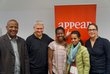 Five people are standing in front of a roll-up, one of them is pointing his finger at it. 