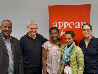 Five people are standing in front of a roll-up, one of them is pointing his finger at it. 