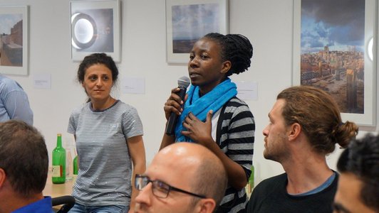 Woman talking into a microphone and other people are looking at her