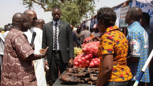 Group of people standing around a table with onions and meat on it and one man talking in a microphone