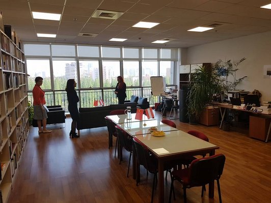 Large room with a table and a large bookshelf and three people standing at the glazed front.