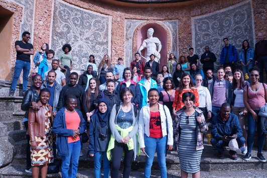 Alle Stipendiaten bei einem Gruppenfoto vor einem großen Wandgemälde mit einer Statue eines Herren.