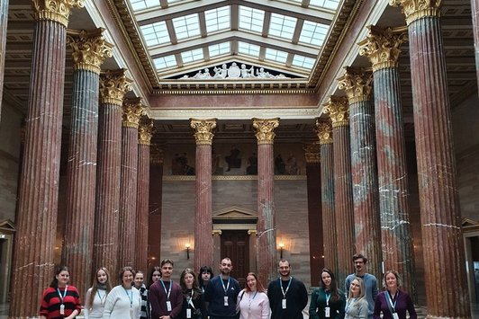 Gruppenfoto in einer Säulenhalle im Parlament, hoher Raum mit einem Dach durch das Tageslicht in die Halle gelangt