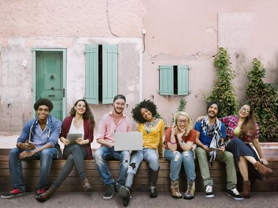 Seven students are sitting on a bench against the wall of a house.