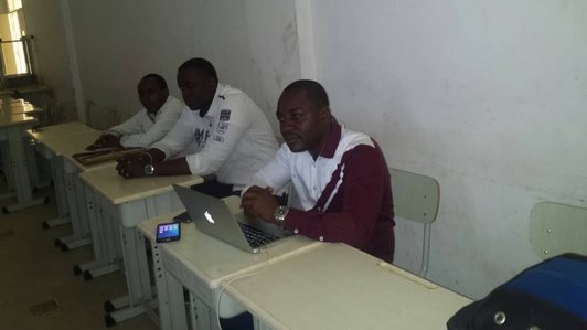 Three man sitting behind white desks, one with a macbook in front of him