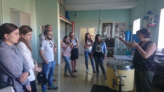 Group of people standing together an looking at awoman who is talking about something in a room with machines