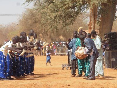 Group of mn in traditional clothing standing in two rows vis-a-vis and wave a beige bushy object