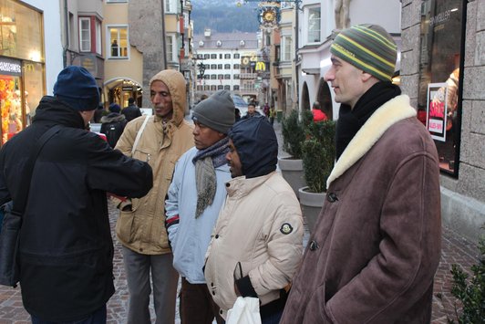 Four man standing in a row and looking at an other man who is showing something