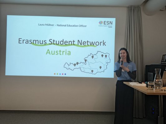 Photo of Laura Müllner, speaker of the Erasmus Student Network (ESN), speaking and presenting a slide