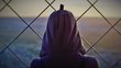 Head of a person with a veil or hood from behind, standing in front of a fence.