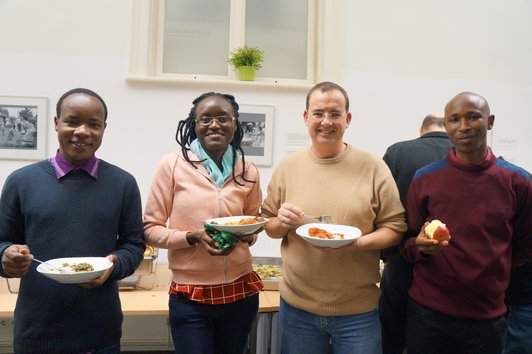 Four people, standing and holding meals in their hands, smiling into the camera.