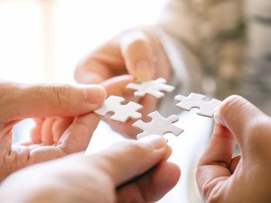 Closeup image of many people holding and putting a piece of white puzzle together