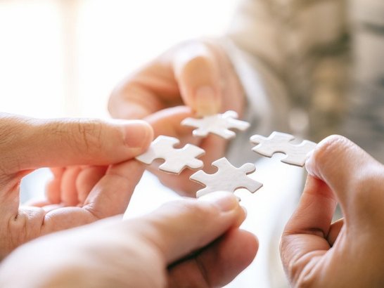 Closeup image of many people holding and putting a piece of white puzzle together