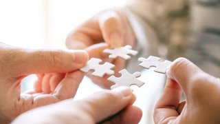 Closeup image of many people holding and putting a piece of white puzzle together