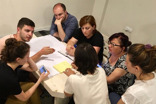 Group of people are sitting together at one table talking to each other, while two persons are looking at their mobile phones