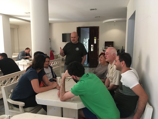 Group of people are sitting around a table while one man is standing and talking