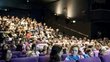 Ein voller Kino Saal mit violetten Sesseln.