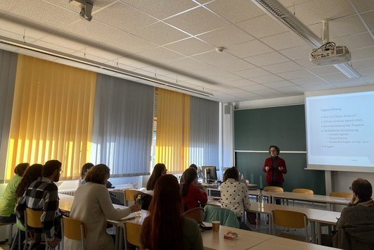 Vortragende vorne an Tafel mit Präsentation, Zuhörende in Tischreihen