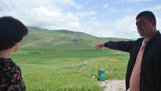 A man and a woman are standing in the midst of a green hilly landscape while the man points at something and the woman is looking in that direction