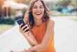 Eine Frau mit einem Telefon in der Hand lacht in die Kamera