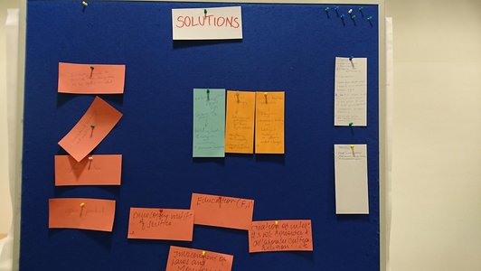 Presentation cards with handwriting on them pinned to a pin board underneath a heading that says "solutions"