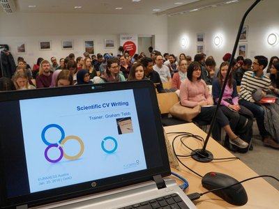 Laptop steht vor einem gut gefüllten Saal im OeAD-Haus: Großer Besucherandrang bei der Veranstaltung.