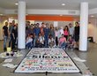  A group of people stand in front of a work of art about silence. In the form of a large fabric square which has been described in several languages.