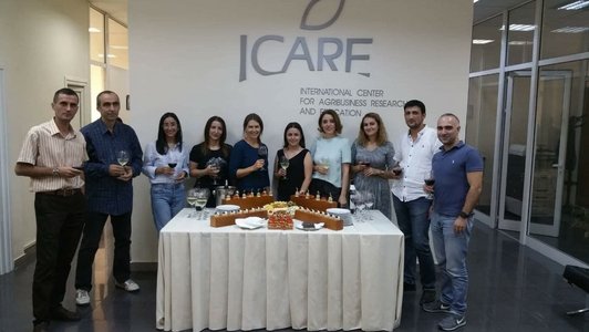Group of people with wineglasses in their hands standing between a buffet table and a big white poster and pose for a picture 