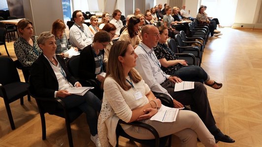 Die Teilnehmenden des Workshops sitzen in drei Stuhlreihen nebeneinander und hören der vortragenden Person zu