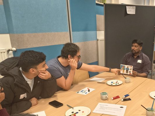 Photo of scholarship holders showing each other pictures they painted and discussing them