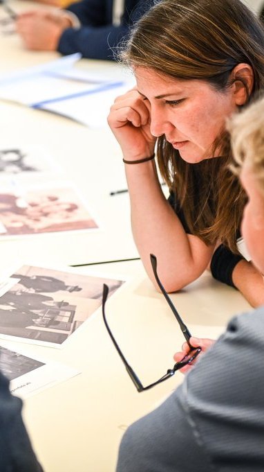 Drei Menschen schauen sich schwarzweiß-Bilder auf einem Tisch - Workshop-Situation