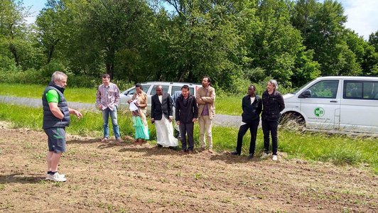 Group of peolple standing on a field in green surrondings with two cars in the background