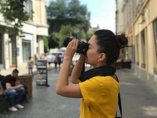 A young woman looks through a reflex camera and takes a photo in the city of Lviv.