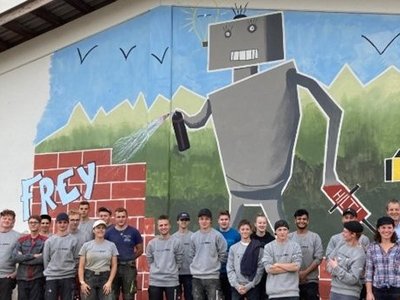  A class in front of a house wall with a spray paint mural.