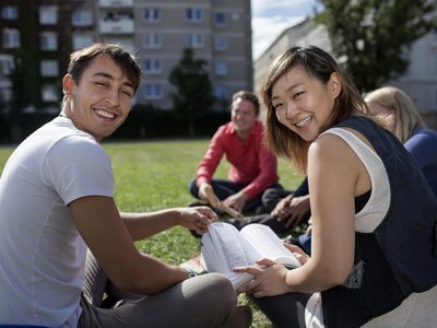  Students sit on the lawn with books and laugh happily