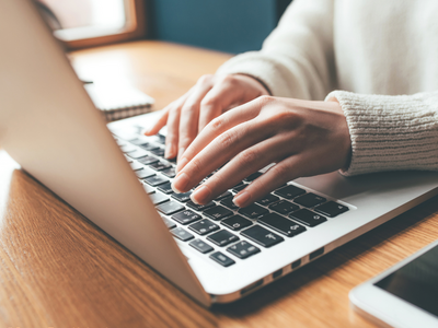 Hände am Laptop arbeitend, daneben liegt ein Smartphone