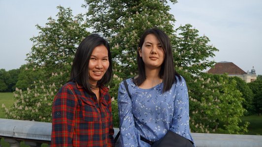 two female students standing in front of some trees in the premises of the Laxenburg park and IIASA institute