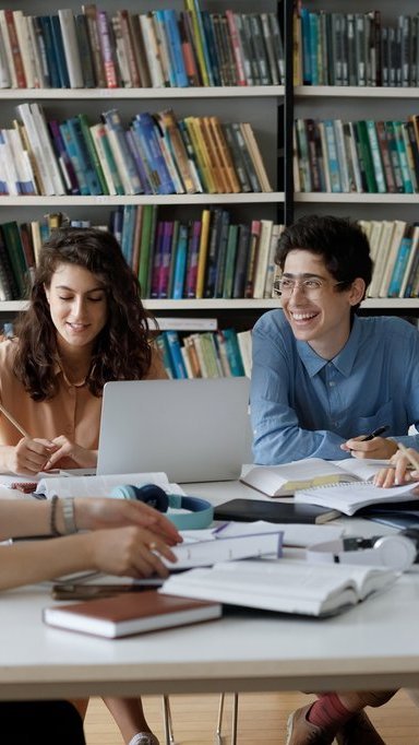 Glückliche vielfältige Gruppe von Studenten, die gemeinsam an einem Studienprojekt arbeiten 