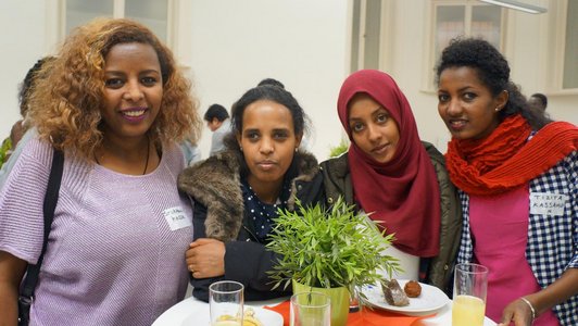 Four women standing behind a bar table with coffee and snacks