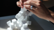  Hands trying to build a tower out of Styrofoam cubes and failing.