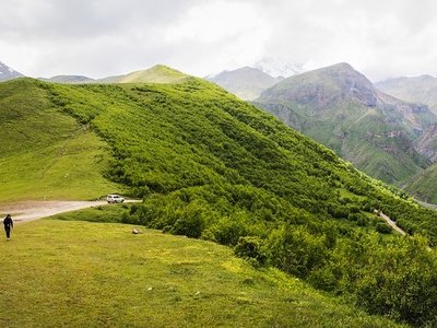 Landschaft im Kaukasus-Gebirge mit grünen Wiesen und Bergen sowie zwei Menschen.