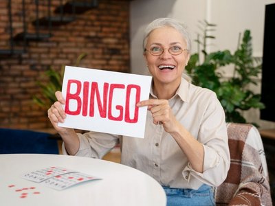 Seniorin mit Bingo-Schild, lächelnd am Tisch